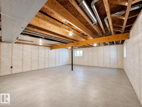 Spacious unfinished basement offering concrete flooring, two visible windows, an exposed wood beam ceiling, and insulated perimeter walls, providing potential for customization - 33 Sumac Close, Fort Saskatchewan, AB 