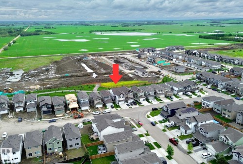 Aerial perspective showcasing a developed residential street with single-family homes, bordered by open fields - 33 Sumac Close, Fort Saskatchewan, AB 