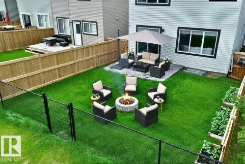 Expansive fenced backyard featuring a stone fire pit, a paved patio with outdoor seating, and raised garden beds - 33 Sumac Close, Fort Saskatchewan, AB 