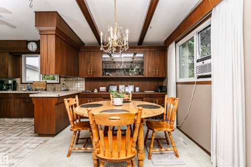 Dining area featuring a brass chandelier, wood-finish ceiling beams, and a window with white drapes - 14231 80 Street, Edmonton, AB 