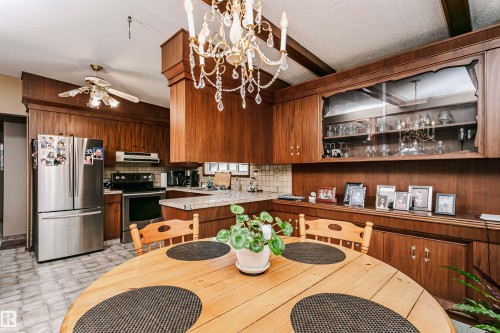Kitchen dining area featuring a chandelier, wood-finish cabinetry, stainless steel appliances, patterned floor tile, and a built-in display cabinet - 14231 80 Street, Edmonton, AB 