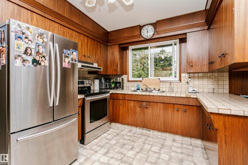 Kitchen featuring wood cabinetry, stainless steel appliances, a tiled countertop, and a tiled backsplash - 14231 80 Street, Edmonton, AB 