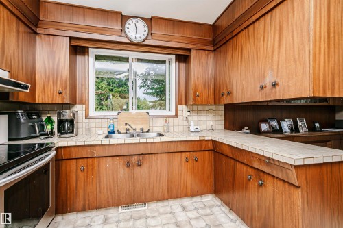 Kitchen featuring wood-finish cabinetry, a double basin sink, tile backsplash, and a tiled countertop - 14231 80 Street, Edmonton, AB 