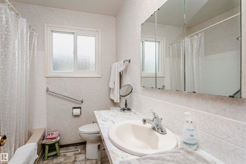 Bathroom featuring a single-pane window with frosted glass, a white toilet, and a white integrated sink set into a laminate countertop - 14231 80 Street, Edmonton, AB 