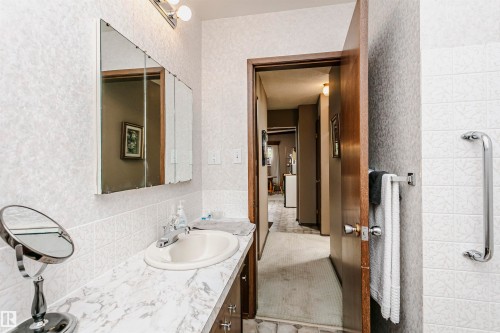 Bathroom vanity with a built-in sink, chrome faucet, and a wall-mounted tri-fold mirror - 14231 80 Street, Edmonton, AB 