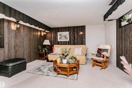 Carpeted room featuring wood-finish paneling and a white painted brick accent wall - 14231 80 Street, Edmonton, AB 