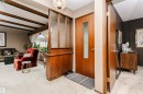 Entryway featuring a wood-finish door with frosted glass insert, an overhead decorative light fixture, and a partial wood-finish room divider with frosted glass panels - 14231 80 Street, Edmonton, AB 