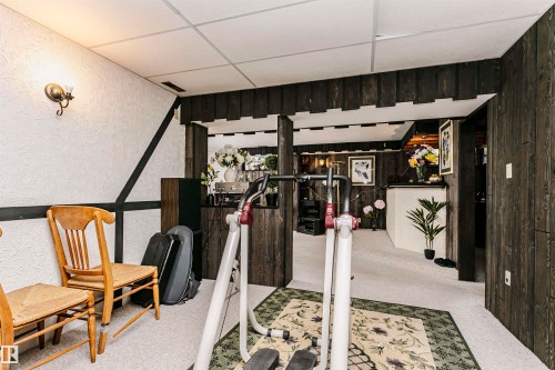 Finished basement space featuring textured white walls with dark trim accents, dark wood-finish wall paneling, light-colored carpeting, and a drop ceiling with integrated lighting - 14231 80 Street, Edmonton, AB 