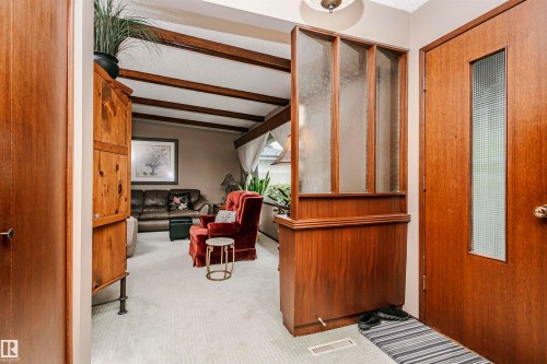 Entryway featuring a wood-panel accent wall with obscured glass panels, a wood-finish entry door with a rectangular obscured glass insert, and neutral-toned carpeting - 14231 80 Street, Edmonton, AB 