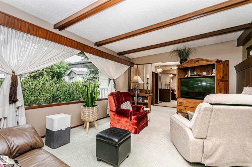 Living area featuring wood-beam ceilings, expansive window with exterior shrubbery, light-toned carpet flooring, and a built-in wood entertainment center - 14231 80 Street, Edmonton, AB 
