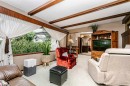 Living area featuring wood-beam ceilings, expansive window with exterior shrubbery, light-toned carpet flooring, and a built-in wood entertainment center - 14231 80 Street, Edmonton, AB 