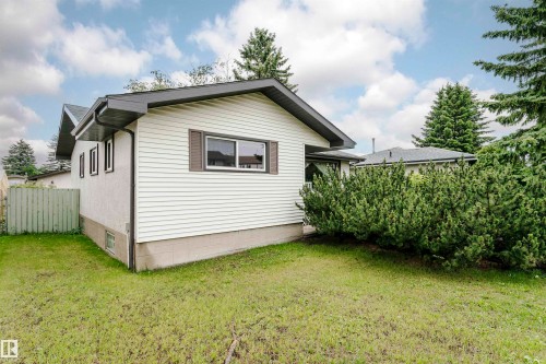 Exterior featuring white siding, a dark roofline, mature evergreen landscaping, and a grassy yard - 14231 80 Street, Edmonton, AB 