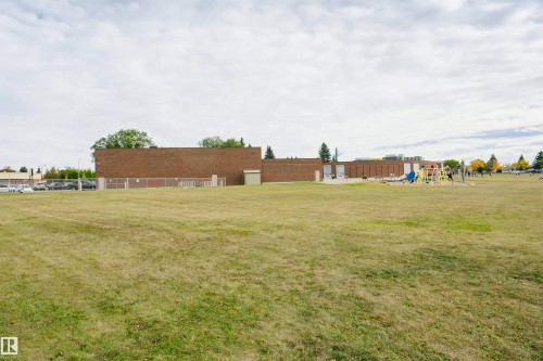 Expansive green space featuring a brick structure, a parking area, mature trees, and a visible playground apparatus - 14231 80 Street, Edmonton, AB 