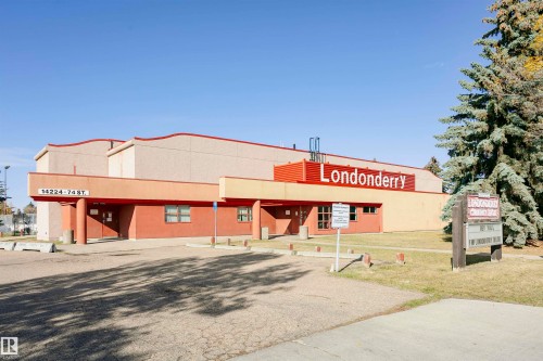 Commercial building with a red and beige facade, featuring multiple entryways, a paved parking area, and a prominent "Londonderry" sign - 14231 80 Street, Edmonton, AB 