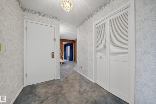 Entryway featuring textured wallpaper, plush carpeting, and a decorative ceiling light fixture - 707 65 Avenue, Edmonton, AB 