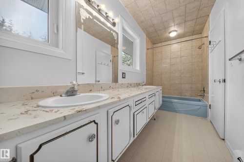 Bathroom featuring a double vanity with stone-finish countertop, dual sinks, and white cabinetry - 707 65 Avenue, Edmonton, AB 