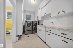 Laundry area featuring light-toned flooring, white cabinetry with ornate hardware, and a window for natural light - 