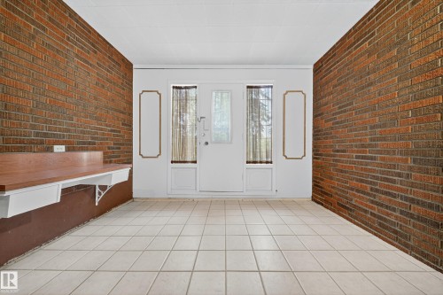 Entryway featuring brick accent walls, light-toned square tile flooring, and a white double door with upper glass panels - 707 65 Avenue, Edmonton, AB 