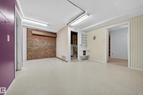 Spacious room with light-colored flooring, exposed brick accent wall, built-in shelving, and multiple doorways - 707 65 Avenue, Edmonton, AB 