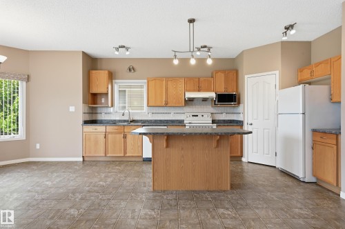 Kitchen featuring wood cabinetry, stone-finish countertops, and a central island - 7460 Singer Landing, Edmonton, AB 