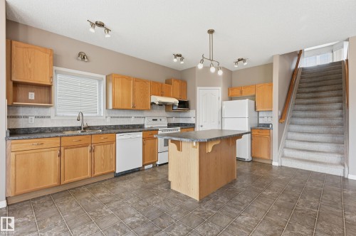 Spacious kitchen featuring warm wood cabinetry, a central island with countertop space, a tiled backsplash, and durable tile flooring - 7460 Singer Landing, Edmonton, AB 