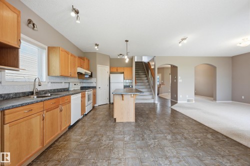 Kitchen featuring wood-finish cabinetry, a central island, and white appliances - 7460 Singer Landing, Edmonton, AB 