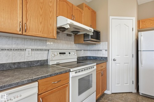 Kitchen with wood-finish cabinetry, white tile backsplash with decorative accent, laminate countertops, and tile flooring - 7460 Singer Landing, Edmonton, AB 