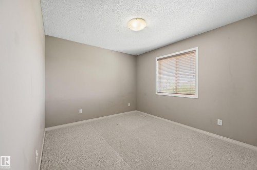 Neutral-toned room featuring a single window with blinds, light-colored carpeting, smooth walls, and a textured ceiling with a flush-mount light fixture - 7460 Singer Landing, Edmonton, AB 