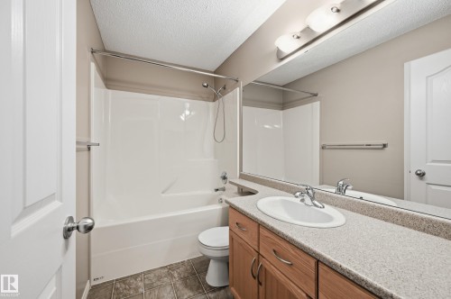 Full bathroom featuring a single vanity with wood-finish cabinetry, a white oval sink, and a speckled countertop - 7460 Singer Landing, Edmonton, AB 