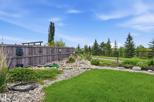 Manicured lawn area with surrounding rock beds, diverse plantings, and a wooden privacy fence - 7460 Singer Landing, Edmonton, AB 
