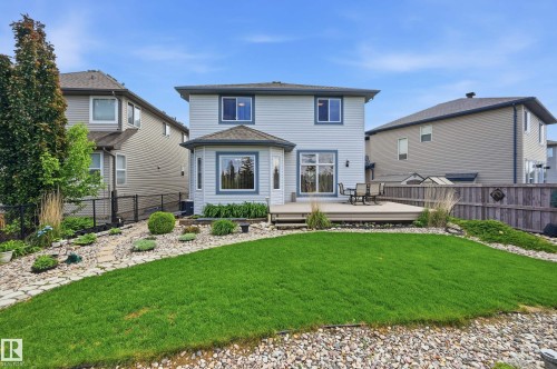 Rear exterior featuring a spacious composite deck, bay window, and a fenced yard with established landscaping and a manicured lawn - 7460 Singer Landing, Edmonton, AB 