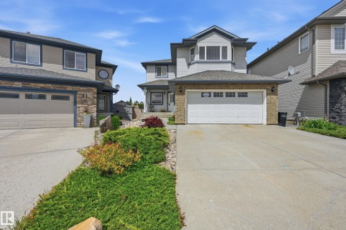 Single-family residence featuring a light-grey siding exterior with stone accents and a multi-car driveway - 7460 Singer Landing, Edmonton, AB 