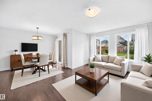 Open-concept living and dining areas featuring wood-finish flooring, abundant natural light from multiple windows, and a sliding glass door providing access to the backyard - 2433 Glenridding Boulevard, Edmonton, AB 