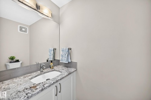 Bathroom vanity featuring a granite countertop with an undermount sink, white cabinetry with dark hardware, a large wall mirror, and a gray subway tile backsplash - 2433 Glenridding Boulevard, Edmonton, AB 