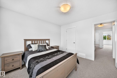 Light-filled bedroom featuring plush carpet flooring, a flush-mount ceiling light fixture, and a white interior door with dark hardware - 2433 Glenridding Boulevard, Edmonton, AB 