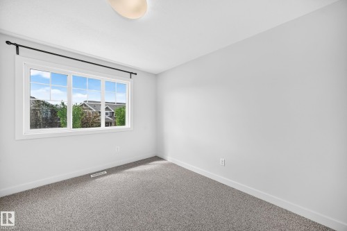 Bright room featuring a large multi-pane window, neutral gray walls, gray carpet flooring, white baseboards, and a flush-mount ceiling light fixture - 2433 Glenridding Boulevard, Edmonton, AB 
