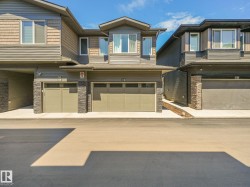 Modern townhouse exterior featuring multi-toned siding, stacked stone accents, multiple large windows, and an integrated garage with a light-colored door - 