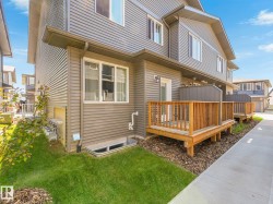 Exterior featuring gray horizontal siding, white trim windows, a ground-level deck with wood railings, and a concrete walkway - 