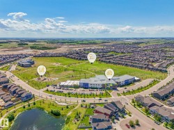 Expansive aerial view of a structured community featuring a central park, a pond, and multiple residential developments - 