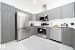 Modern kitchen featuring light gray shaker cabinetry, stainless steel appliances, white subway tile backsplash, white countertops, and wood-finish flooring - 