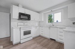 Modern kitchen featuring white shaker-style cabinetry, a built-in microwave, white electric range, and a window above the sink - 