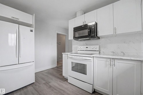Kitchen featuring white cabinetry with brushed nickel hardware, complementing white appliances, a built-in black microwave, and a white marble-patterned backsplash - 12707 87 Street, Edmonton, AB 