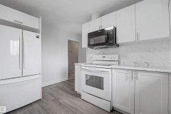 Kitchen featuring white cabinetry with brushed nickel hardware, complementing white appliances, a built-in black microwave, and a white marble-patterned backsplash - 