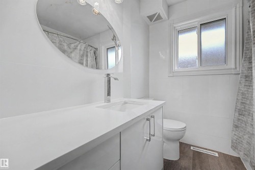 Modern bathroom featuring a white vanity with an integrated sink, chrome faucet, and oval mirror - 12707 87 Street, Edmonton, AB 