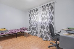 Bright interior space featuring light wood-finish flooring, white walls, and a window with patterned drapes - 