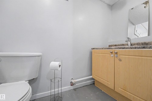 Bathroom featuring a light wood-finish vanity with a speckled countertop, a rectangular mirror, a chrome faucet, and a toilet - 12707 87 Street, Edmonton, AB 
