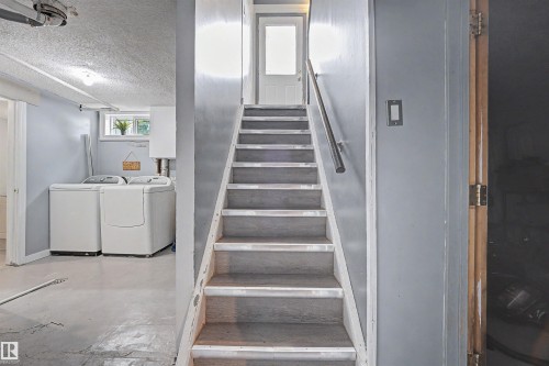 Staircase with a metal handrail leading to an upper level, alongside a laundry area featuring a window and overhead lighting - 12707 87 Street, Edmonton, AB 