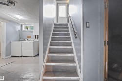 Staircase with a metal handrail leading to an upper level, alongside a laundry area featuring a window and overhead lighting - 