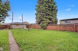 Spacious fenced backyard featuring a detached garage, mature trees, and a concrete pathway - 
