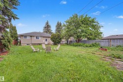 Expansive rear yard featuring a large mature tree, perimeter fencing, and a stucco exterior with multiple windows - 